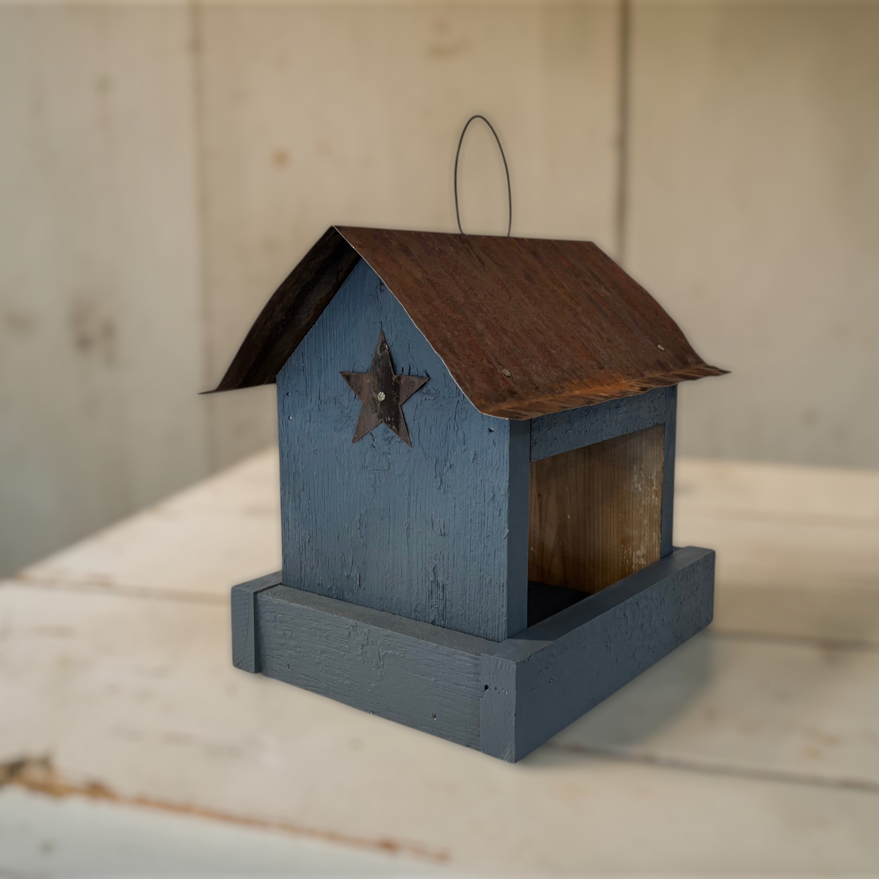 Rustic  blue wooden birdfeeder with a tin roof and star on both ends. Tray for easy feeding.