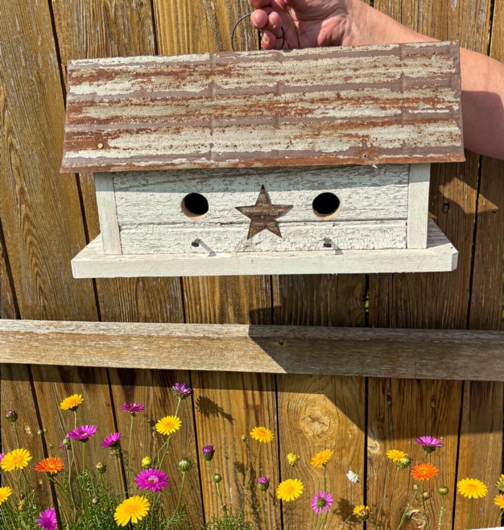 Wooden birdhouse with a star design on a wooden fence with flowers in the foreground