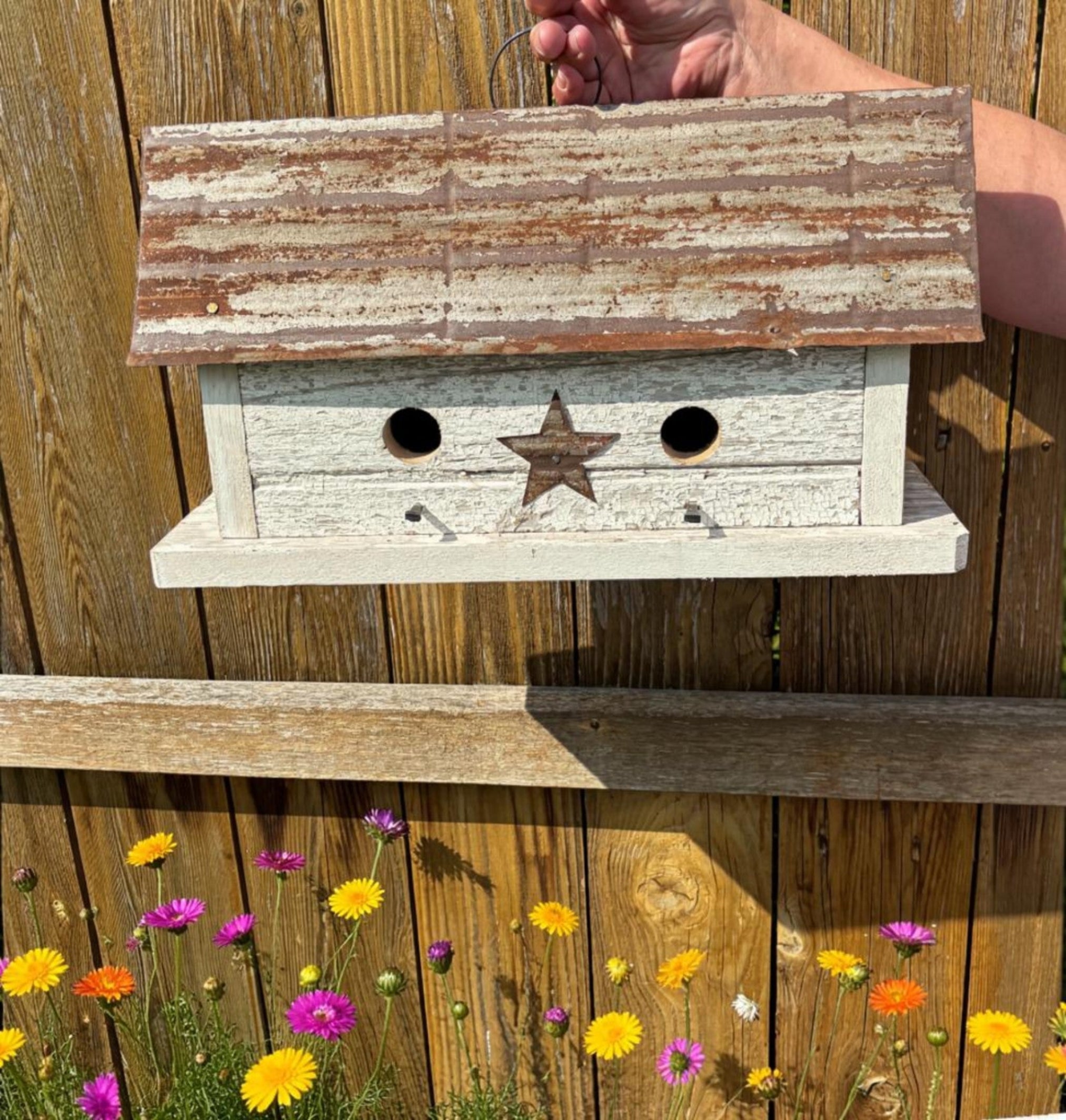 Wooden birdhouse with a star design on a wooden fence with flowers in the foreground